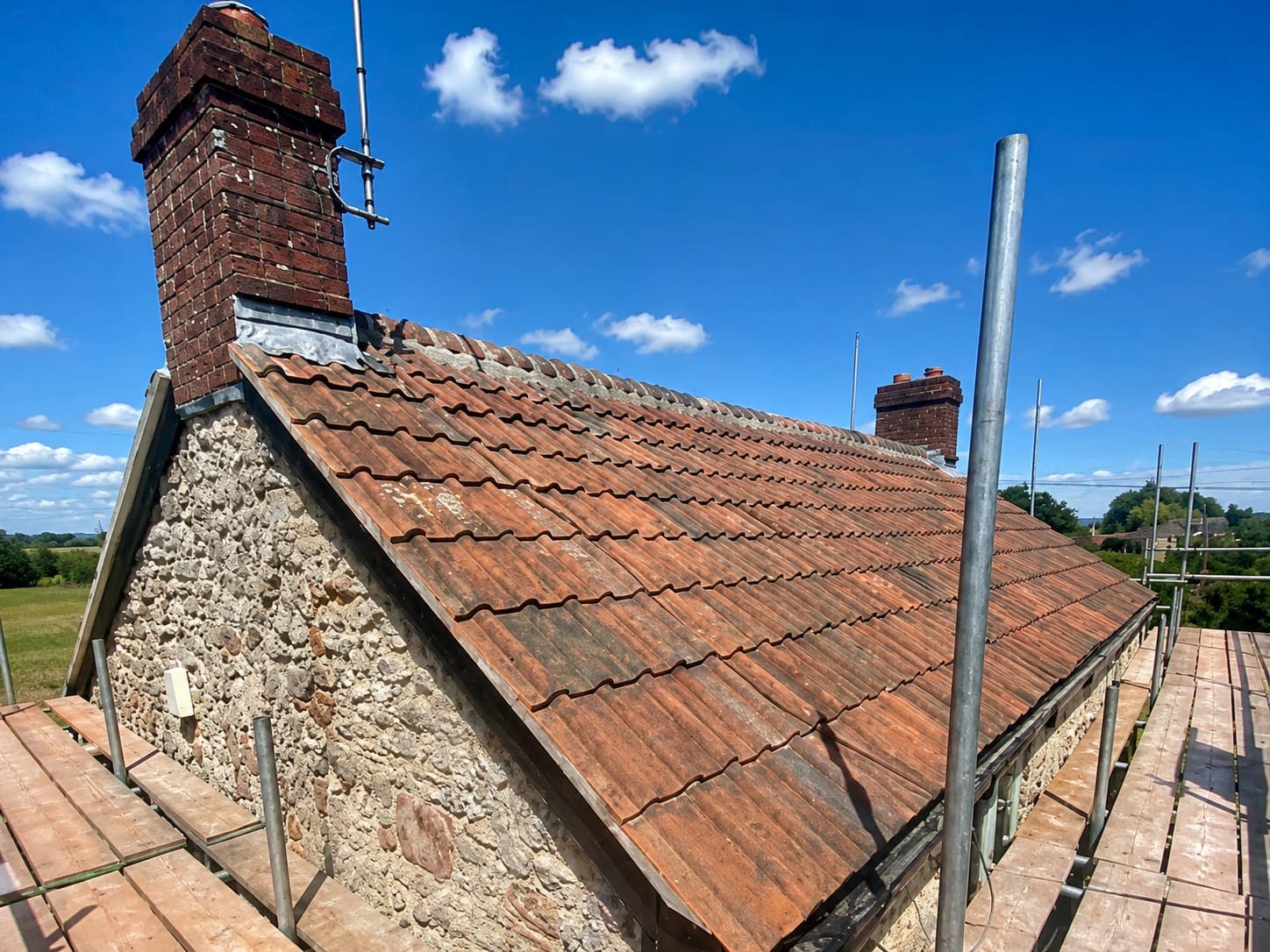 Clay pantile roof and brick chimney on a stone cottage, with open countryside behind