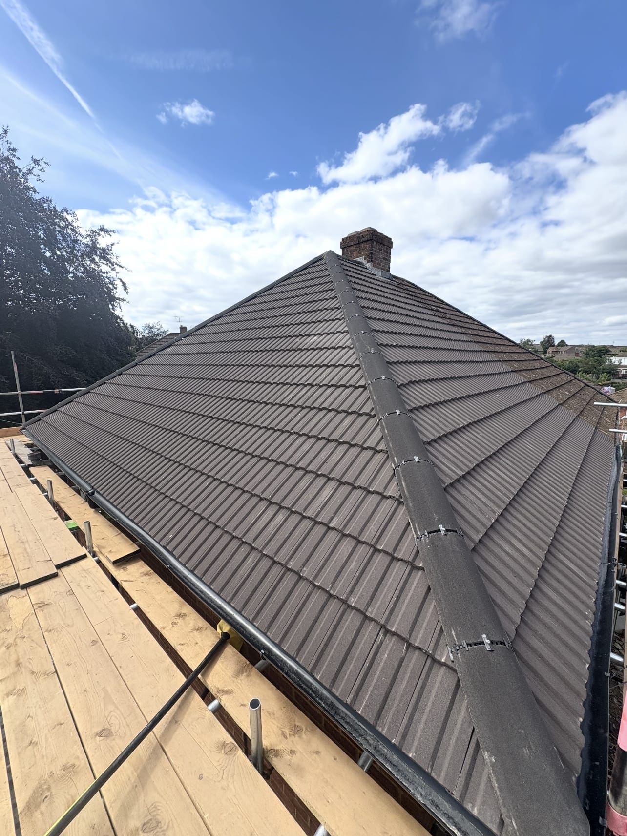 Completed hipped roof in dark grey tiles with a dry ridge and hip system, seen from the scaffold